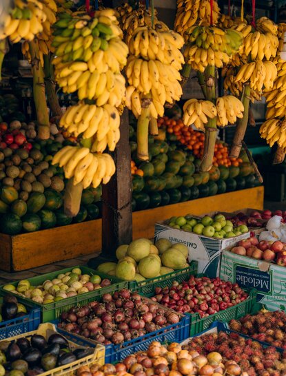 Bunches of golden bananas hanging above colourful produce at a local market in Amangalla, Sri Lanka.