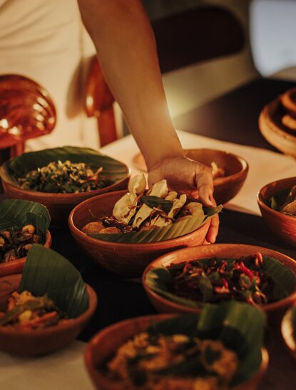 Hand reaching for traditional Sri Lankan dish at Amangalla's communal dining table.