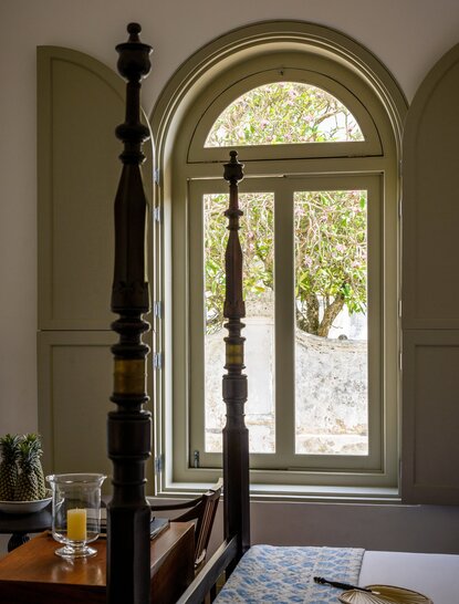 Arched doorway with glass panels opening onto garden at Amangalla, Sri Lanka, with wooden bedpost in foreground.