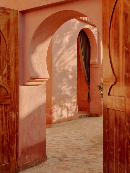 Terracotta-toned corridor with arched doorways at Amanjena, Morocco.
