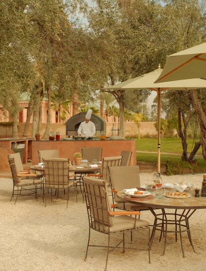 Amanjena's olive grove with outdoor seating beneath ancient trees and cream parasols.