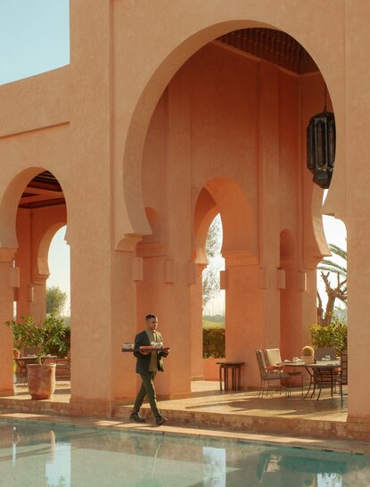 Main pool at Amanjena, Morocco, framed by terracotta archways and still water.