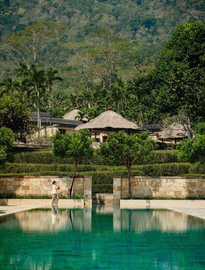 Amanjiwo's stone pool pavilions overlook emerald waters with forested hillside beyond.