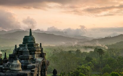 Amanjiwo temple overlooks mist-covered Kedu Valley at dawn, surrounded by verdant hills.