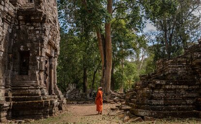 Buddhist monk walking amongst ancient temple ruins at Angkor, Cambodia.