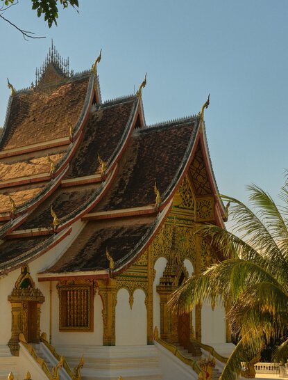 Golden-roofed temple with tiered spires at Amantaka, Laos, framed by tropical foliage.