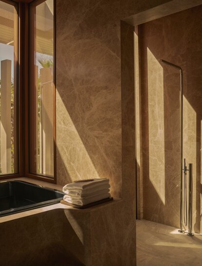 Sunlit corridor in an Estuary Casita at Amanvari, Mexico, with warm earthy walls and geometric shadows cast through tall windows.