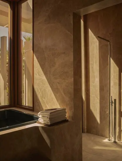 Sunlit corridor in an Estuary Casita at Amanvari, Mexico, with warm earthy walls and geometric shadows cast through tall windows.