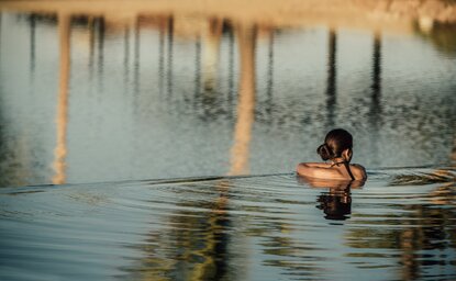 Guest swimming in still water at Amanvari, Mexico, with wooden posts reflected in the surface.