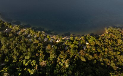 Camp area at Amanwana in the morning light, with tropical forest canopy overlooking dark waters.