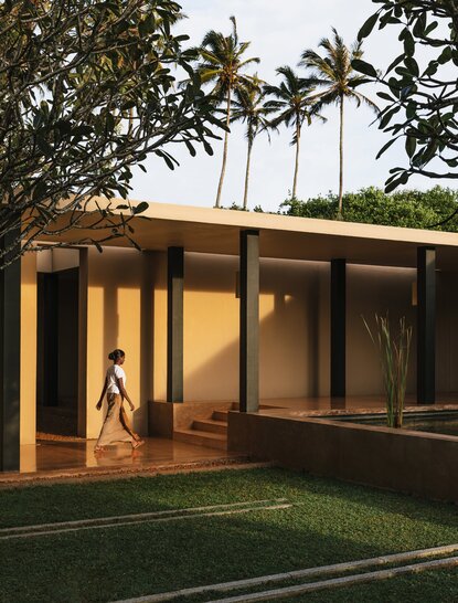 Wooden pavilion with glass doors at Amanwella, Sri Lanka, framed by palm trees at dusk.
