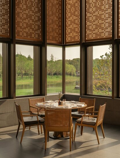 Dining area at Amanyangyun with wooden table and chairs, framed by large windows overlooking rural landscape.