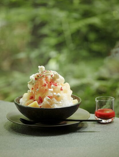 Shaved peach ice dessert topped with cream at Aman Tokyo lounge, served with red syrup.
