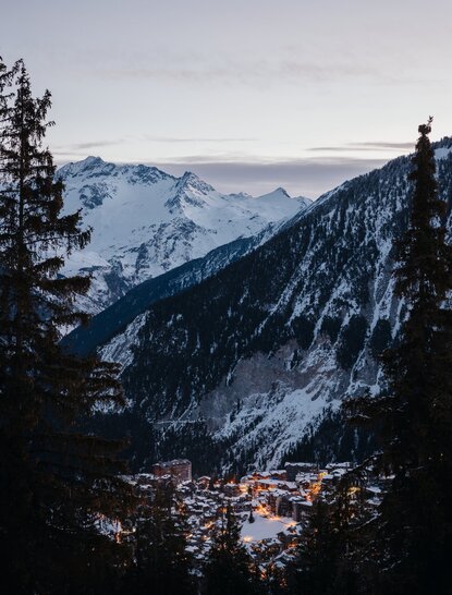 Courchevel town nestled in a snow-covered Alpine valley at dusk, with mountains rising beyond.