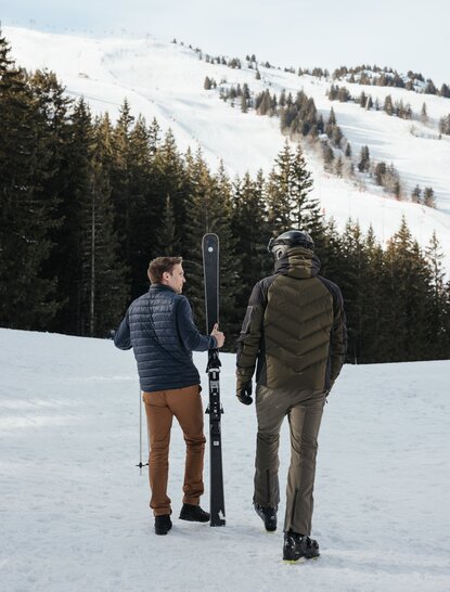 Two people walking across snowy landscape at Aman Le Mélézin, French Alps.