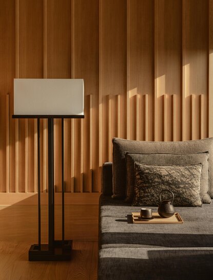 Wooden-slat accent wall with floor lamp and bed at Aman Tokyo accommodation.