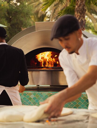 Chef preparing pizza at Amanjena's wood-fired oven during dining experience.