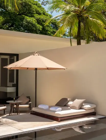 Amansara pool suite exterior with sunbed, parasol and palm trees.