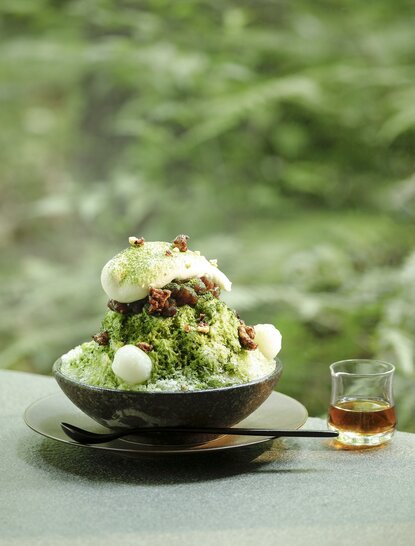 Matcha shaved ice dessert at Aman Tokyo, topped with white cream and served in a dark bowl.