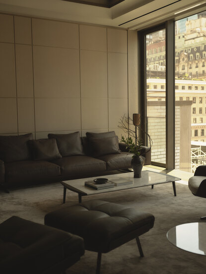 Salon d'une chambre au 17e étage à Aman New York, avec canapé noir, vue sur la ville et fenêtres panoramiques.