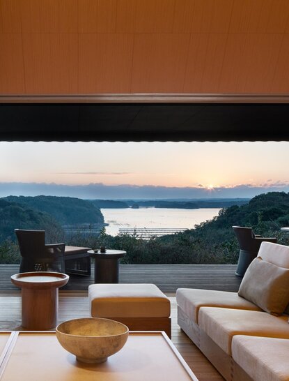 Sora Villa living area at Amanemu overlooking coastal mountains at dusk, with contemporary seating and expansive windows.