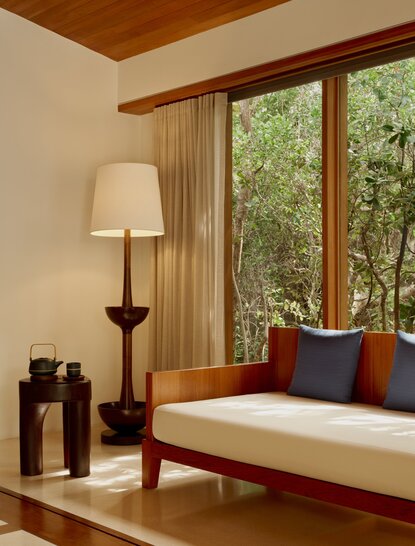 Alcove pool pavilion living area at Amanyara with daybed, floor lamp and garden views through large windows.