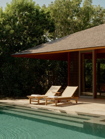 Wooden sun loungers beside an ocean-view pool pavilion at Amanyara, surrounded by tropical vegetation.