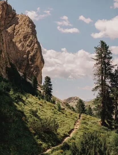 Cyclist riding through lush Alpine valley beneath towering rock formations at Aman Rosa Alpina, Italy.