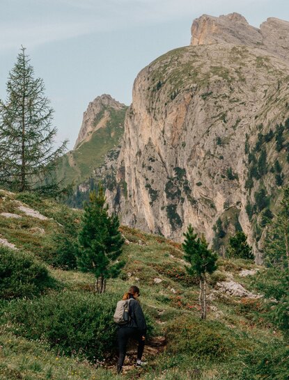 Hiker on a mountain trail at Aman Rosa Alpina resort, with dramatic rocky peaks and alpine forest.