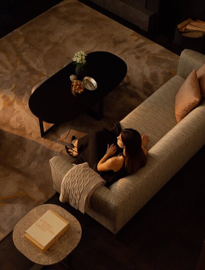 Il Salotto at Aman Rosa Alpina resort, viewed from above, shows a guest relaxing on a cream sofa with warm lighting.