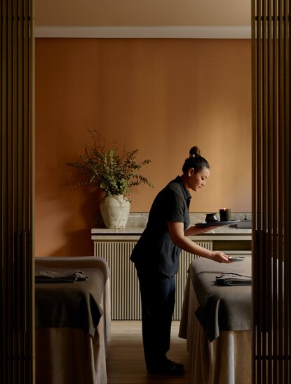 Woman in black attire at a wooden desk in a warm, minimalist wellness space at Aman New York.