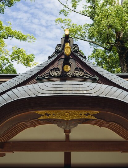 Curved roof detail of a traditional Japanese structure at Amanemu resort, with ornamental gold finial against green foliage.