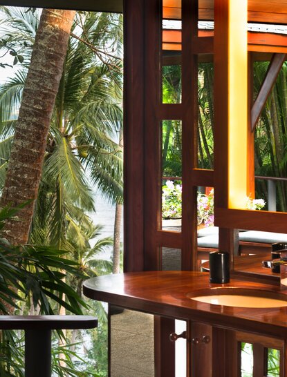 Ocean Pavilion bathroom at Amanpuri, Thailand, with wooden cabinetry and tropical garden views through open shutters.