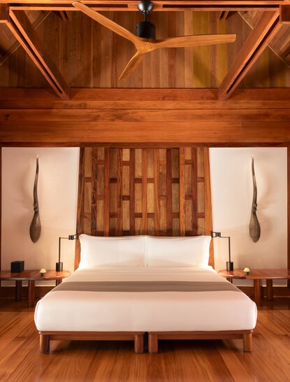 Amanpuri bedroom with wooden walls, geometric wall panels and pendant lights flanking a bed.