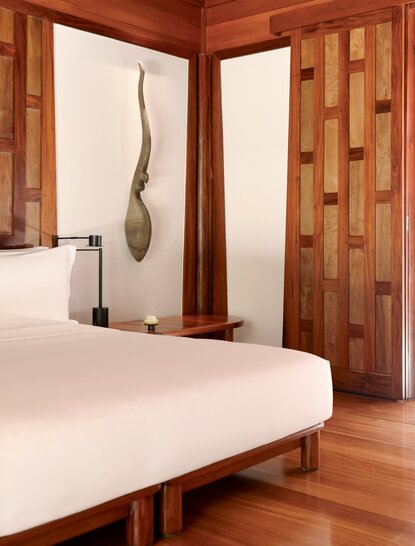 Amanpuri pavilion bedroom with warm timber walls, platform bed, and minimalist décor.