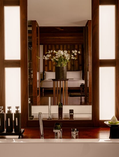 Amanpuri bathroom pavilion interior with wooden vanity, dark cabinetry and illuminated mirror panels.