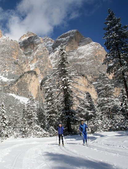 Dolomites snow-covered landscape with two figures in blue standing on a snowy path at Aman Rosa Alpina resort.