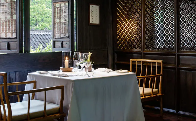 Amanfayun dining room with round table set for service, wooden chairs, and dark panelled walls with latticed windows.