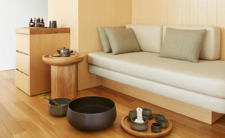 Amanemu wellness retreat space with minimalist daybed, wooden furniture and meditation bowl.