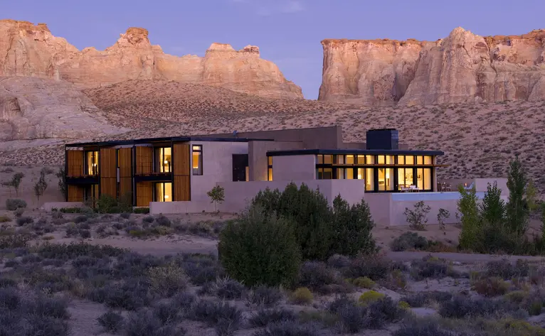 Mesa Home at Amangiri illuminated at dusk, set against towering red rock formations in the Utah desert.