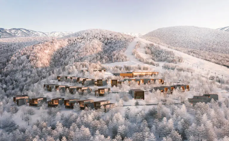 アマン ニセコ リトリート&ヴィラズの空撮。雪に覆われた山々に囲まれた冬景色の中、リゾート施設が広がる。
