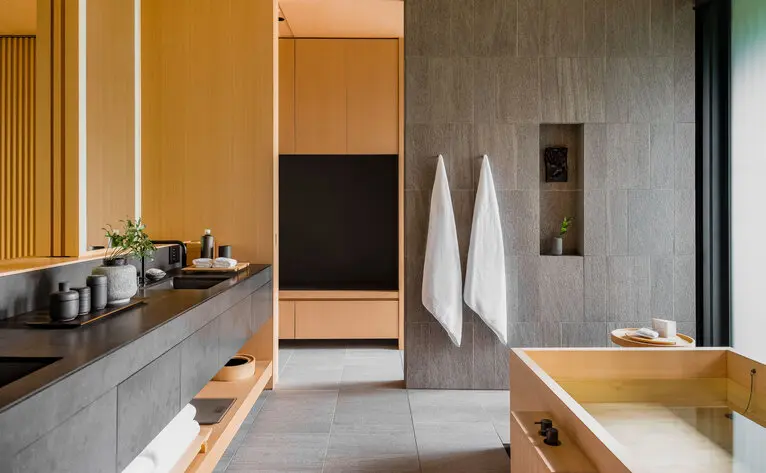 Salle de bains spacieuse avec baignoire en bois, comptoir en pierre et éclairage naturel à Aman Kyoto.