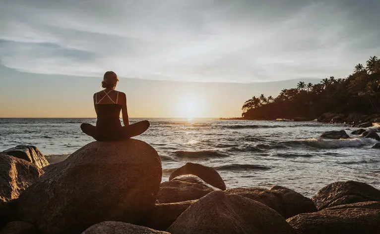 Personne assise sur un rocher face à la mer au coucher du soleil, Amanpuri.