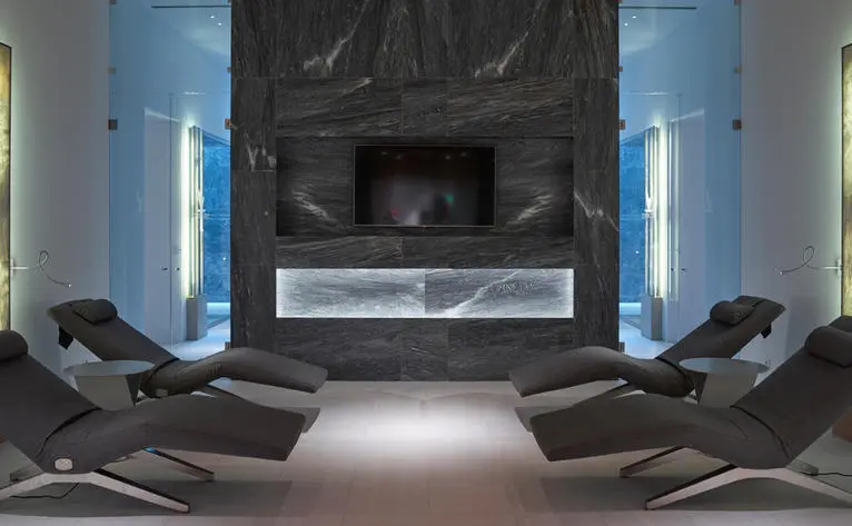 Contemporary spa relaxation area at Amanzoe with curved charcoal loungers facing a central fireplace.