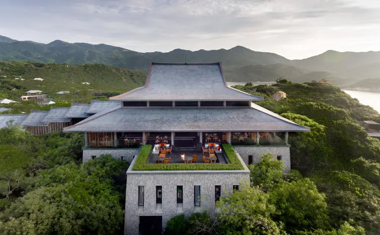 Amanoi's central pavilion overlooks verdant coastline and mountains under clouded skies.