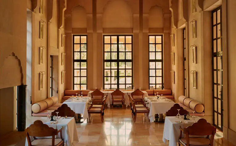 Amanbagh restaurant with tall arched windows, wooden chairs, and warm terracotta tones.