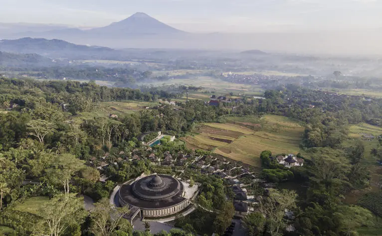 Aerial view of Amanjiwo resort nestled among terraced rice fields and volcanic landscape in Indonesia.