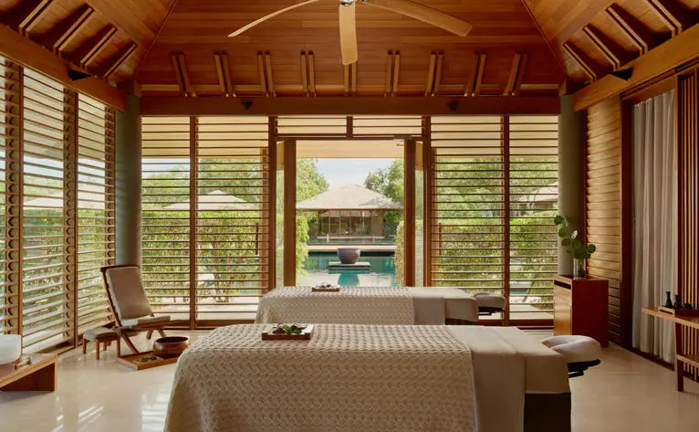 Wellness room at Amanyara resort with wooden ceiling, floor-to-ceiling windows overlooking tropical gardens, and soaking tub.