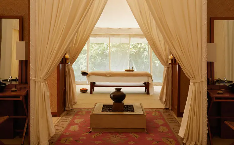 Spa interior at Aman-i-Khas with wooden treatment bed, flowing curtains and views across Indian landscape.