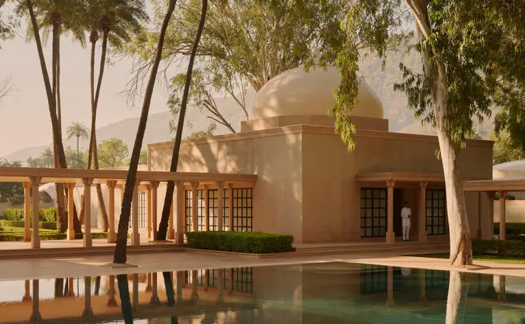 Amanbagh's main spa building reflected in a still pool, framed by palm trees at dusk.